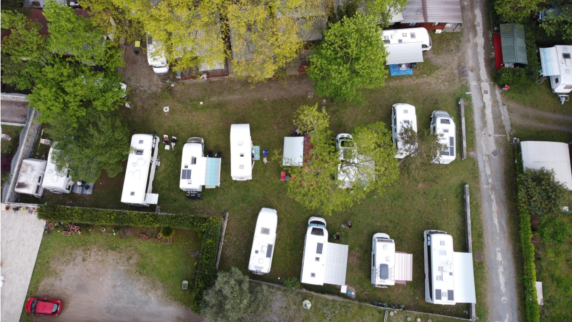 Vista aerea di camper parcheggiati in un campeggio verde con alberi.