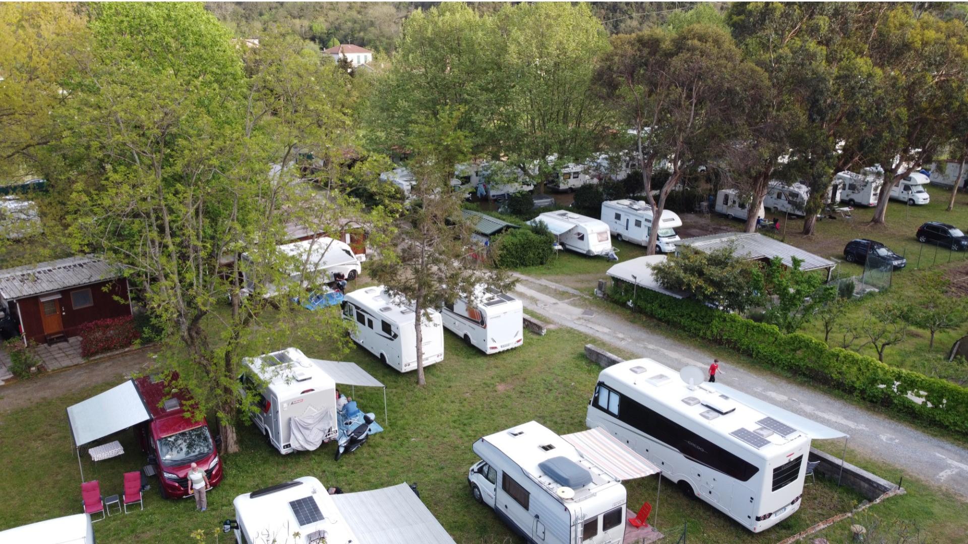 Aire de repos pour camping-cars entourée de verdure avec de nombreux arbres.
