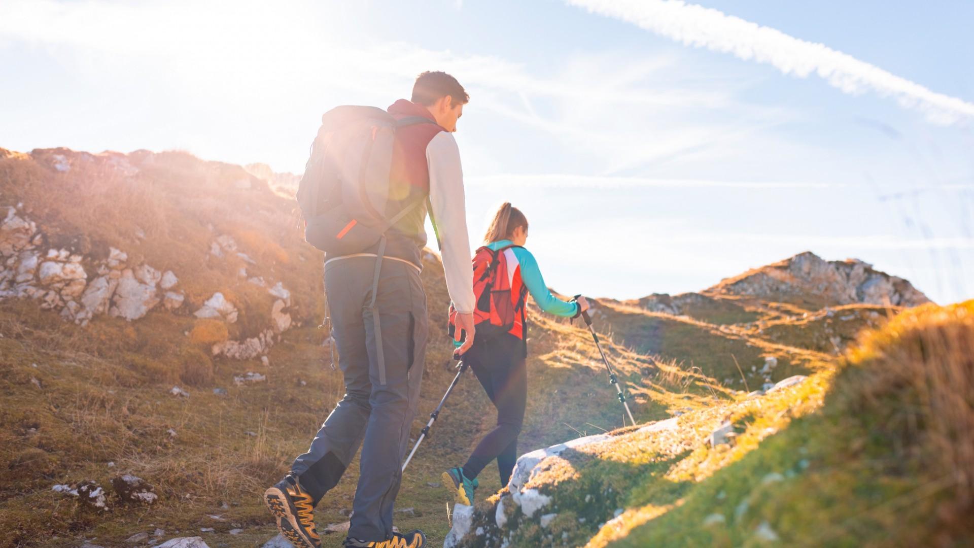 Due persone fanno escursioni su un sentiero montano al tramonto.
