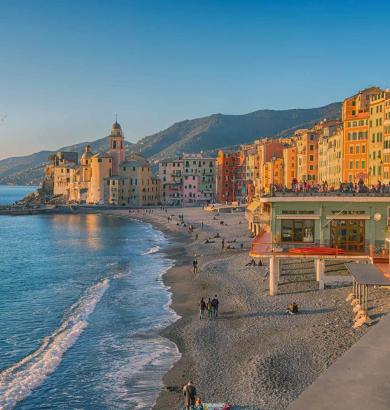 Spiaggia con edifici colorati e chiesa sul mare, colline sullo sfondo.