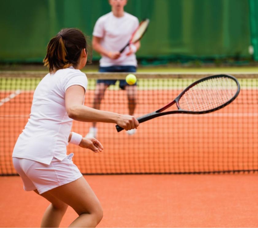 Due persone giocano a tennis su un campo in terra rossa.